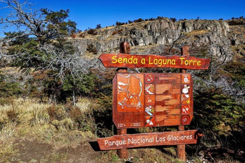 Detailed wooden sign with directions to Laguna Torre in front of a rocky landscape with autumnal