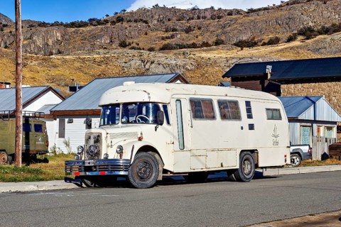 A vintage camper van parked in a mountainous landscape, surrounded by houses and clear skies, A