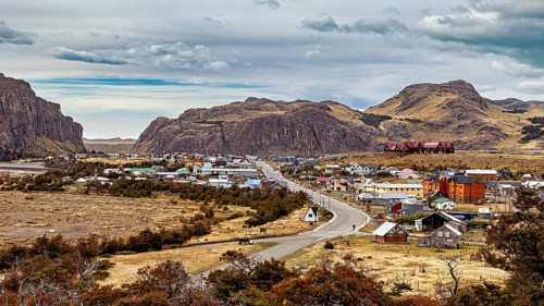 A small village nestled in a hilly landscape along a winding road, the village of El Chalten in
