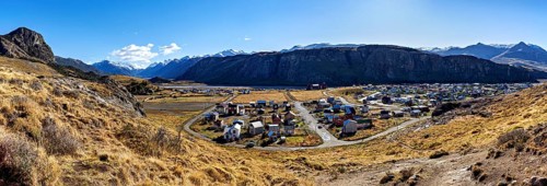 Panoramic view of a village in the valley, surrounded by high mountains and dry grassland under a