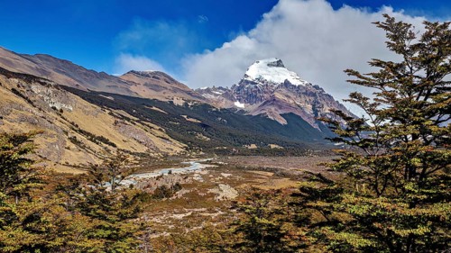 Wide valley with a river, surrounded by mountain peaks and wooded areas, The Patagonian landscape