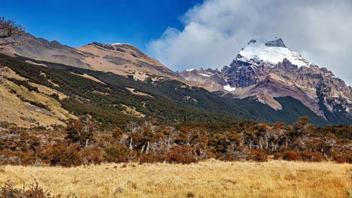 Mountain landscape, snow-covered peaks with wooded slopes and exposed rocks under a blue sky, The