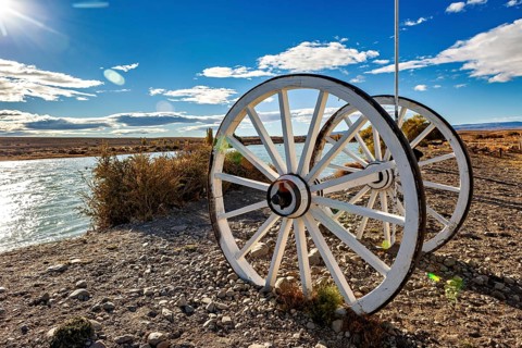 White wagon wheels on the riverbank under a blue sky with clouds, Historic horse-drawn wagon or