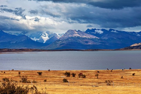 The peaceful, wide lake surrounded by mountains under a dramatic sky, The Patagonian landscape near