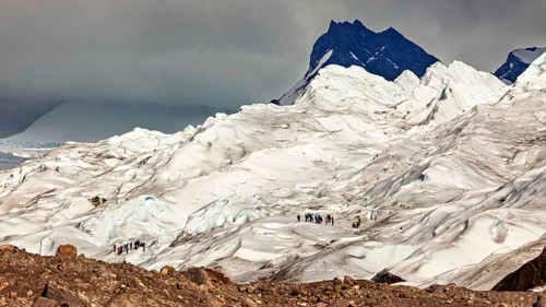 A group of people hiking on a glacier, surrounded by a harsh, icy landscape and dark mountains in