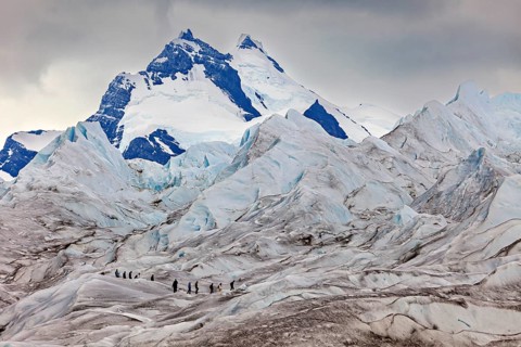 Adventurous climbers on a glacier with looming mountains and clouds, The Perito Moreno glacier in