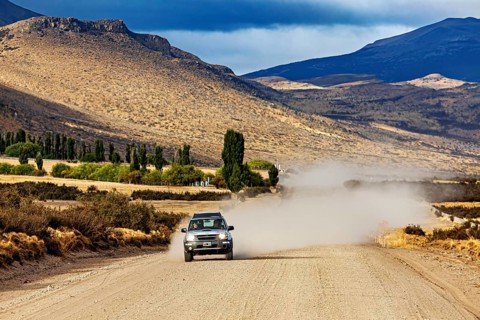 A car drives on a dusty gravel road through a mountainous landscape, Over gravel tracks through