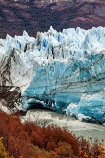 An imposing glacier stretches through a mountainous landscape, surrounded by autumn-coloured trees
