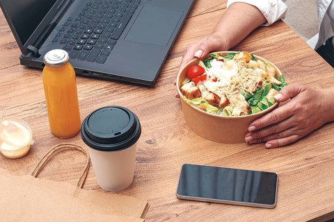 A woman is working on a laptop at home, there is food on the table, salad, coffee and juice,