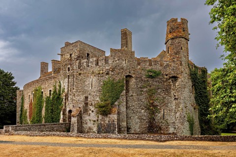 Stone castle with round towers and ivy growth under a cloudy sky, Pirou Castle in Normandy, France