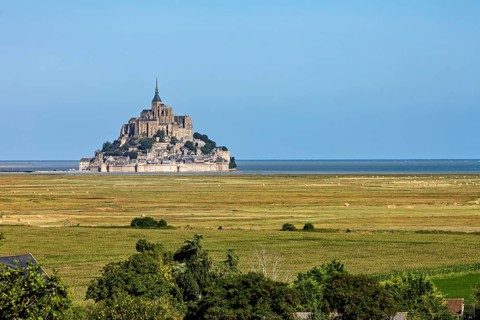 Historic abbey on a rocky island off the coast of France, surrounded by green fields and blue
