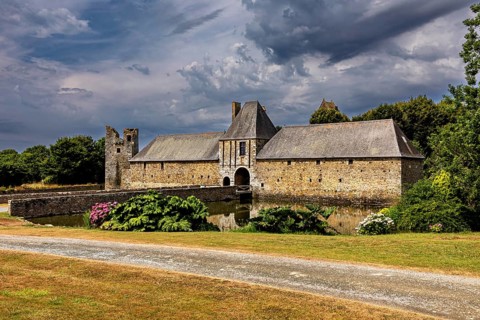 Historic castle with moat and garden under a dramatic sky, Gratot Castle in Normandy, France