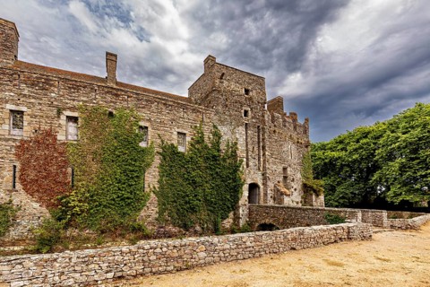 Side view of an old castle with ivy, under a cloudy sky, Pirou Castle in Normandy, France