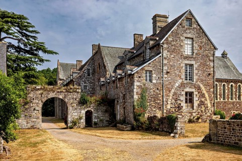 A historic stone building with archway and vegetation under a cloudy sky, The Abbey de La Lucerne