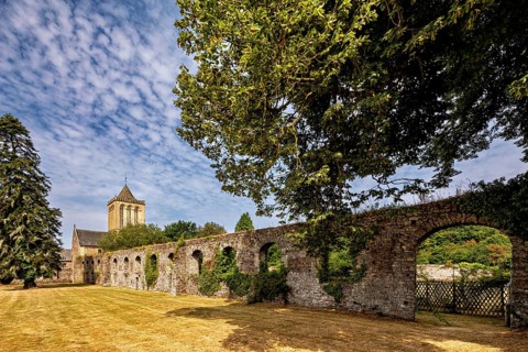 A vast stone wall next to a church, surrounded by trees under a clear sky, The Abbey of La Lucerne