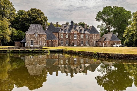 A historic castle behind a tranquil pond with a reflection and trees, The Abbey de La Lucerne in