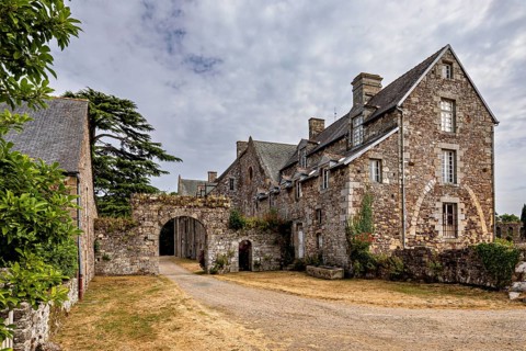 Historic stone building with an archway under a cloudy sky in a rural setting, The Abbey de La