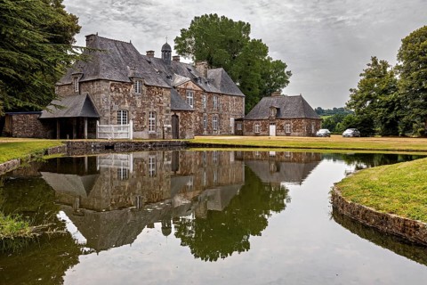 A castle with a pond in front of it, in which the building and the surrounding trees are reflected,