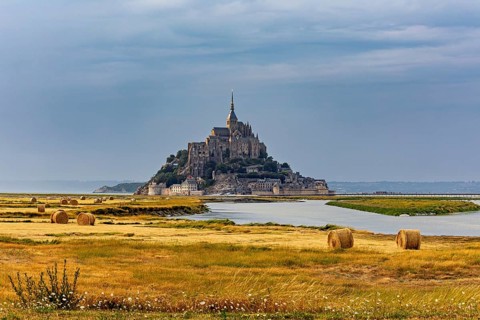 A castle island with ecclesiastical architecture in a rural landscape under a cloudy sky, Mont