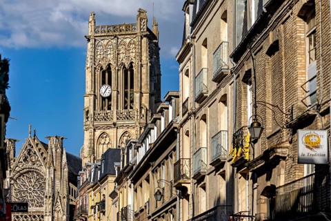 Gothic cathedral with impressive bell tower and stone architecture along the street under a blue