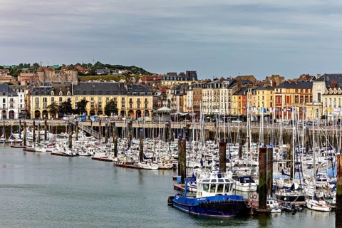 Cityscape with harbour and boats in front of a hilly backdrop under a cloudy sky, The harbour of