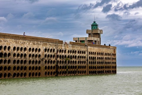 Long harbour wall with lighthouse, surrounded by the sea, under a sky with clouds, The harbour pier