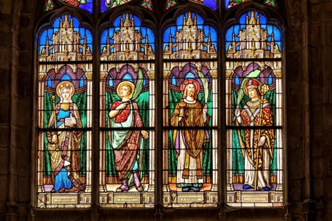 A Gothic church window shows colourful depictions of angels and saints in detailed stained glass,