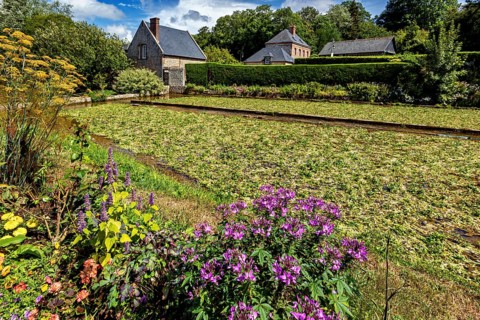 Lush flower bed in front of a charming brick house in a summery, rural setting, The historic mill