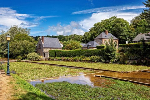 Sprawling fields with brick houses under a blue sky, surrounded by green nature, the historic mill