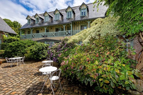 Lively garden with flowers and seating areas, surrounded by a backdrop of half-timbered houses, the