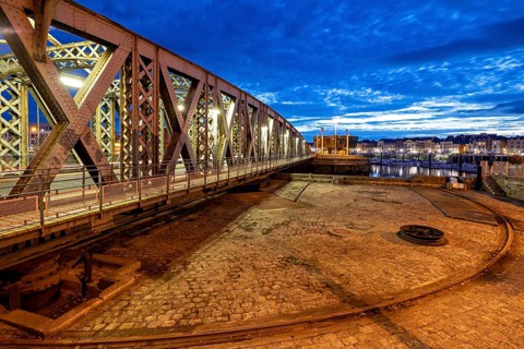 Metal bridge in evening city with illuminated sky and cloudy horizon, The swing bridge of Dieppe in
