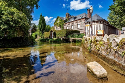 A water-rich courtyard with a historic building and vegetation under a blue sky, the historic mill