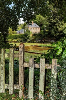 A cosy house behind an old, overgrown garden fence in a rural setting, the historic mill village of