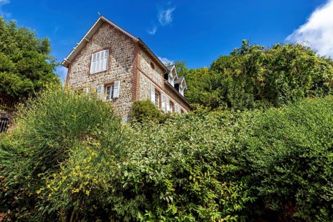 Single brick house behind green bushes and trees under a clear blue sky, The historic mill village