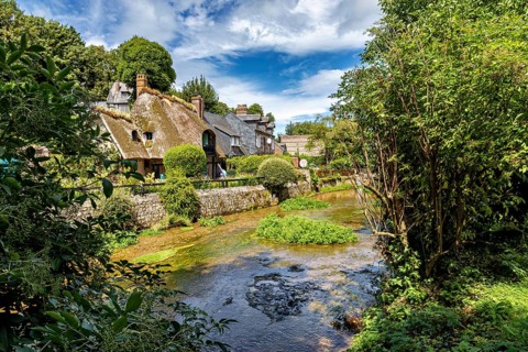 Half-timbered house in the middle of an idyllic landscape with a flowing stream and lush greenery,