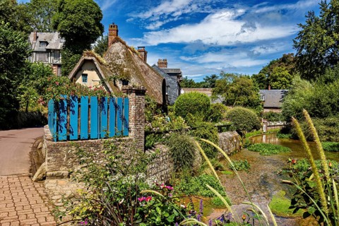 Thatched roof house with blue fence on a path surrounded by natural, picturesque landscape, The