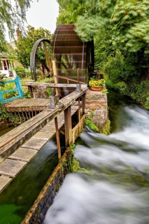 Old waterwheel next to a rushing river, surrounded by lush greenery and wooden bridges, the