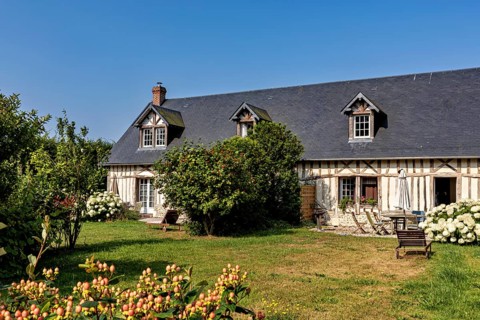 Cosy half-timbered house with flowering shrubs and green meadow under a clear sky, Historic houses