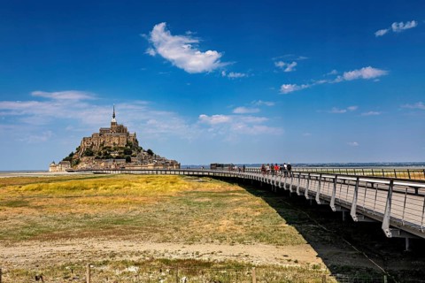 A medieval castle with a long wooden bridge under a clear blue sky, Mont Saint Michel in Normandy,