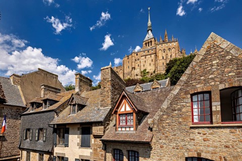 Stone and tiled roofs of ancient buildings with a dominant tower in the background under a clear