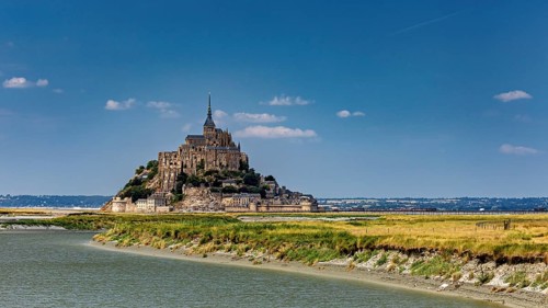 A majestic castle perched on the riverbank under a sunny sky, Mont Saint Michel in Normandy, France