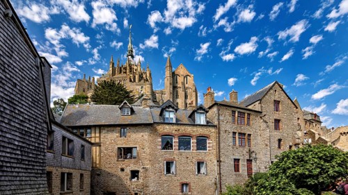 Historic stone architecture with a view of a castle under a blue sky with decorative clouds, Mont