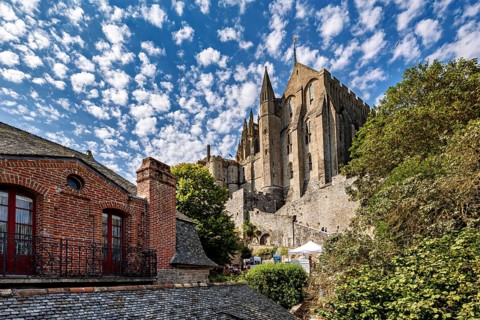 View of an imposing medieval castle against a cloudy sky, surrounded by green trees and old