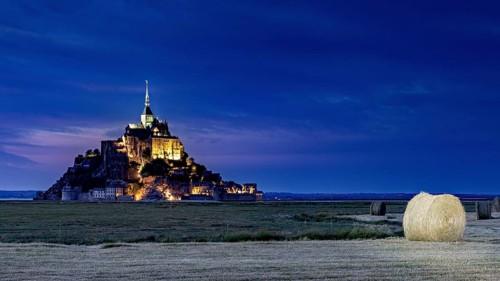 Mont Saint-Michel at night with a bale of hay in a field in the foreground, Mont Saint Michel in