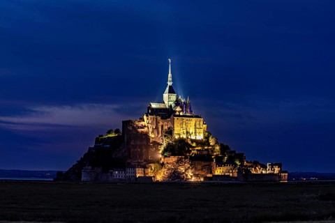 Historic monastery illuminated at night against a dark blue sky, Mont Saint Michel in Normandy,