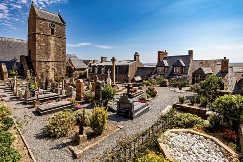 A peaceful cemetery next to a church with gravestones and flowers under a clear blue sky, The