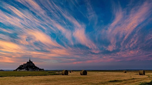 Mont Saint-Michel at sunset with dramatic sky and straw bales, Mont Saint Michel in Normandy,