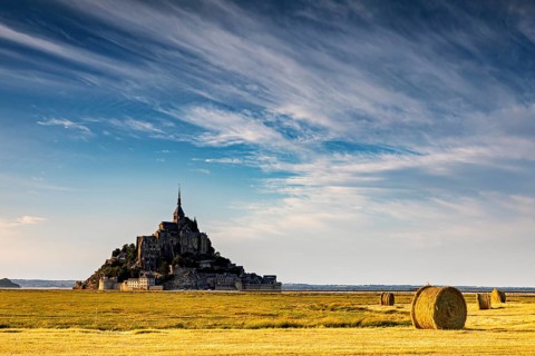 Mont Saint-Michel with dramatic sky and bales of straw in a wide field, Mont Saint Michel in