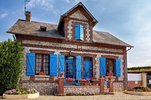 Historic stone house with blue shutters and blooming flowers in decorative plant beds, Historic
