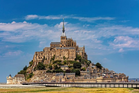 An imposing castle rises against a blue sky with a few clouds, Mont Saint Michel in Normandy,